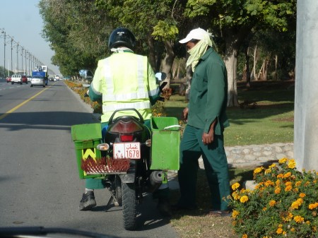 The Ministry Pulic Works registers some motorcycles for transport of gardeners to the far reaches of the towns, to the parks, highway verges and floral roundabouts.    Here an inspector checks on a Tamil labourer near the airport.     Brumby archive